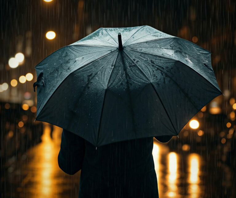 person holding a black umbrella while walking down a rain-soaked city street at night.
